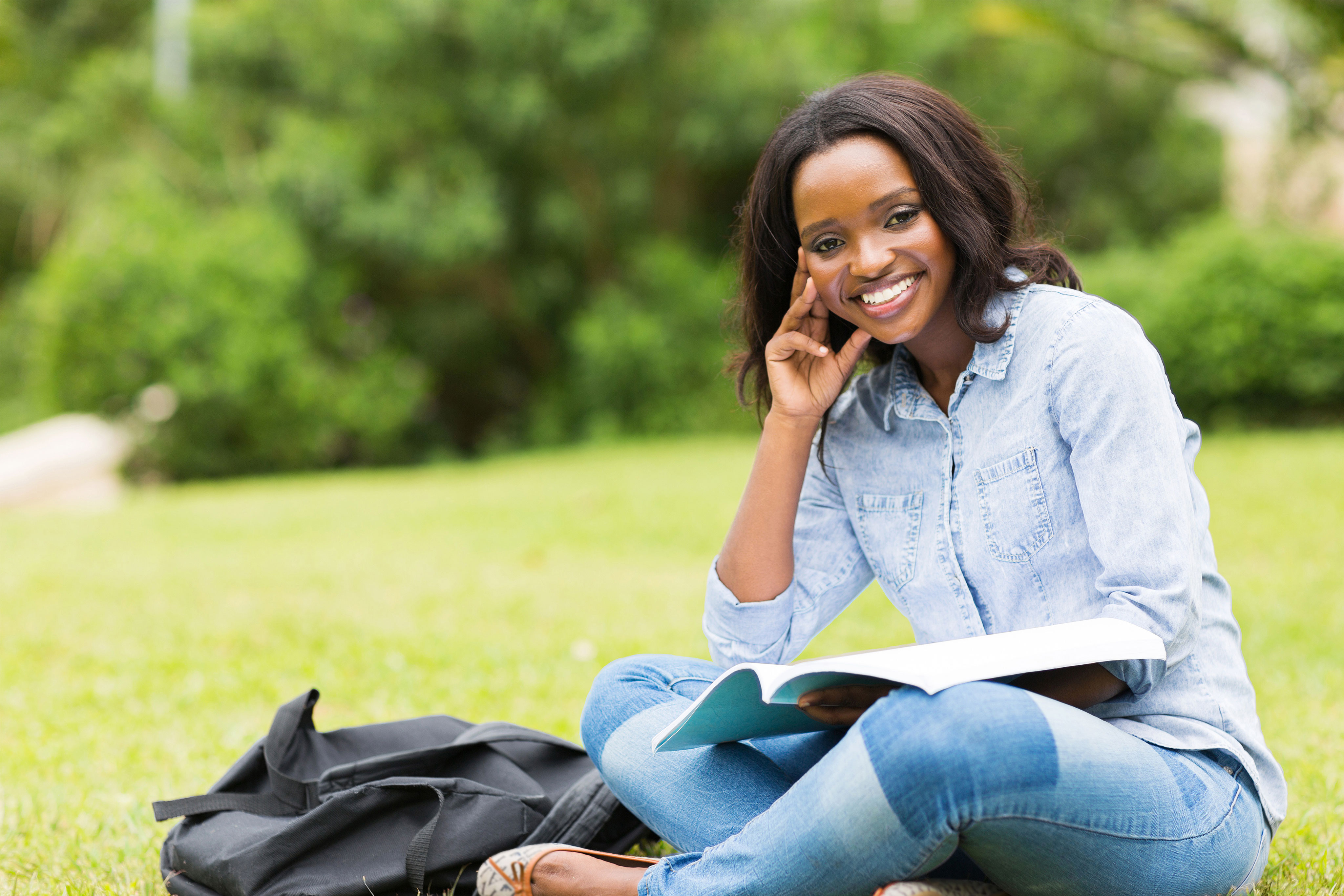 woman sitting on grass, holding book, smiling