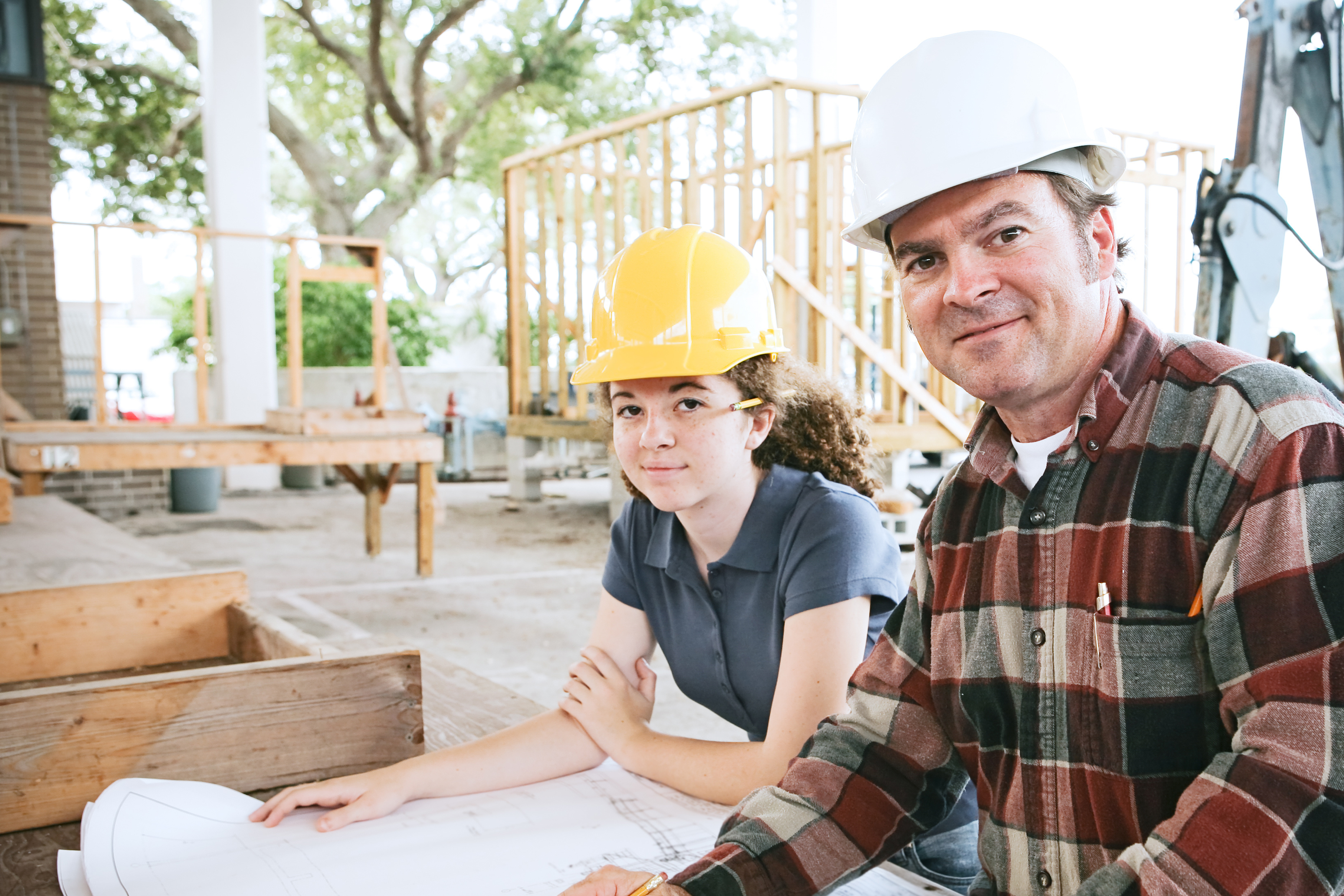young woman and older man wearing hard hats and looking at blueprints