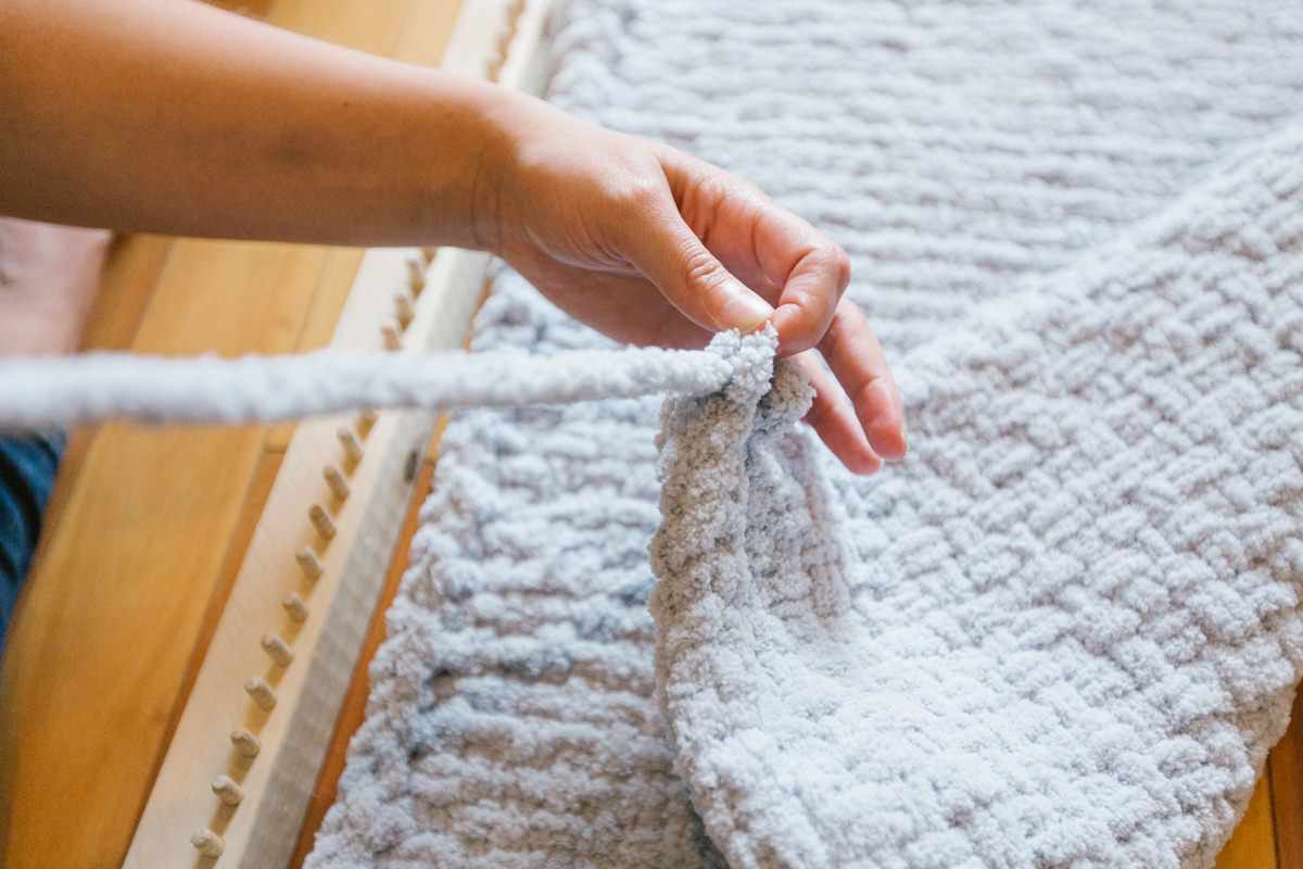 Holding up long yarn tail of rug made on DIY wooden rug loom.