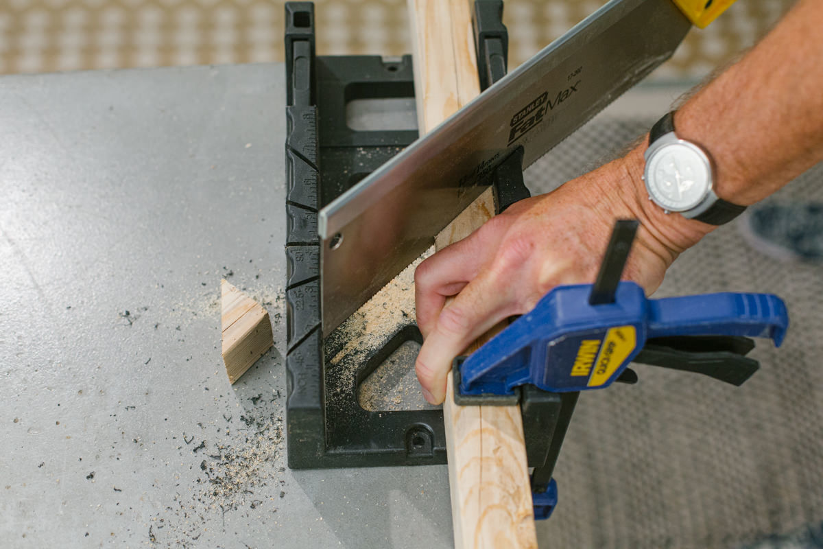 Cutting clamped lumber in miter box with handsaw.