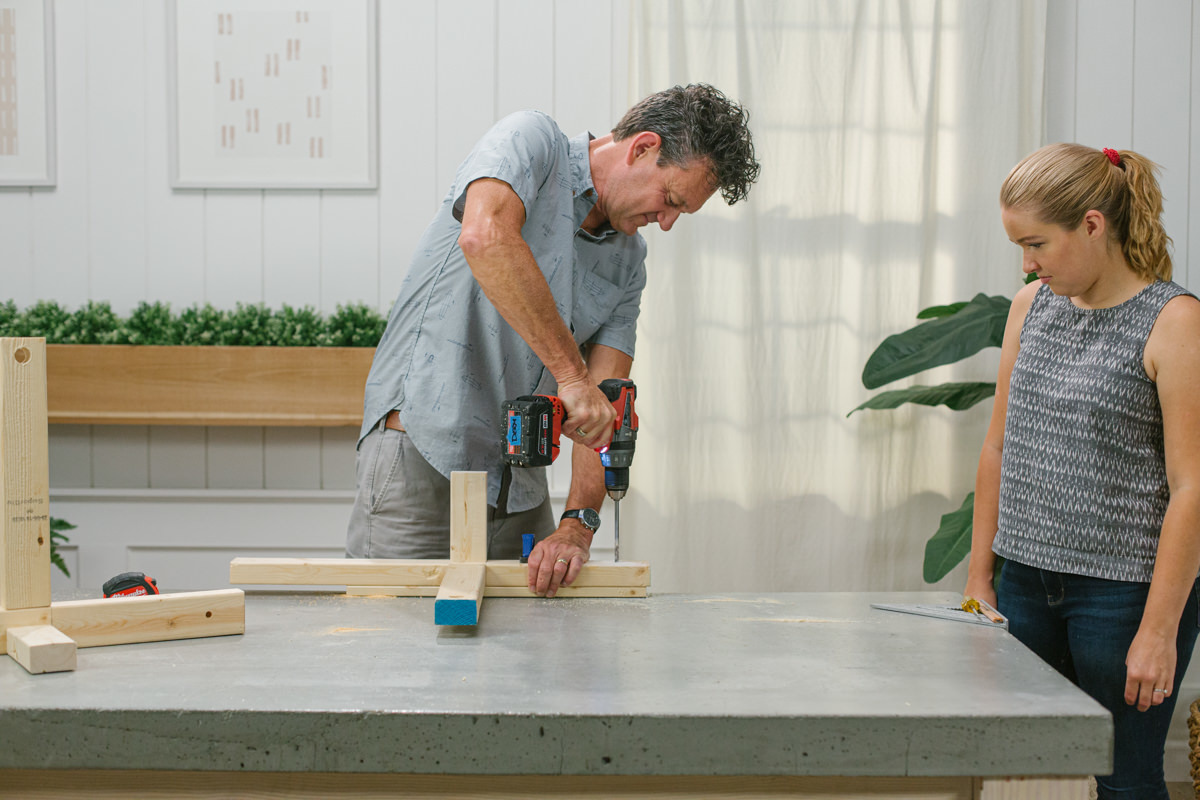 Drilling hole in clamped base of DIY wooden mini trebuchet side assembly.