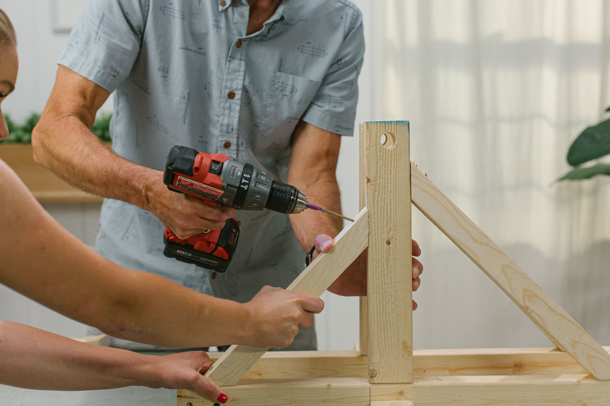 Driving screw with power drill to attach front braces to DIY wooden mini trebuchet assembly.