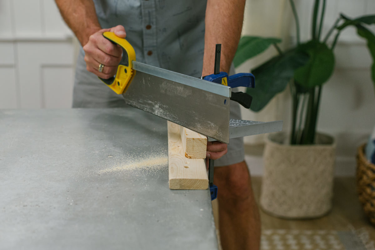 Cutting clamped board with handsaw.