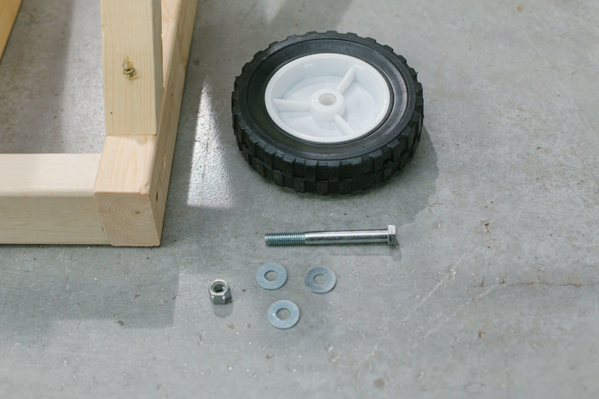 Wheel, bolt, washers and stop nut laid out next to DIY wooden mini trebuchet assembly.