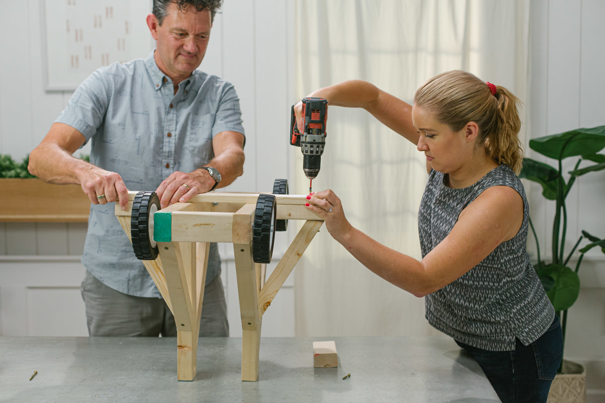 Driving screw with power drill to attach frame support to base of DIY wooden mini trebuchet assembly.