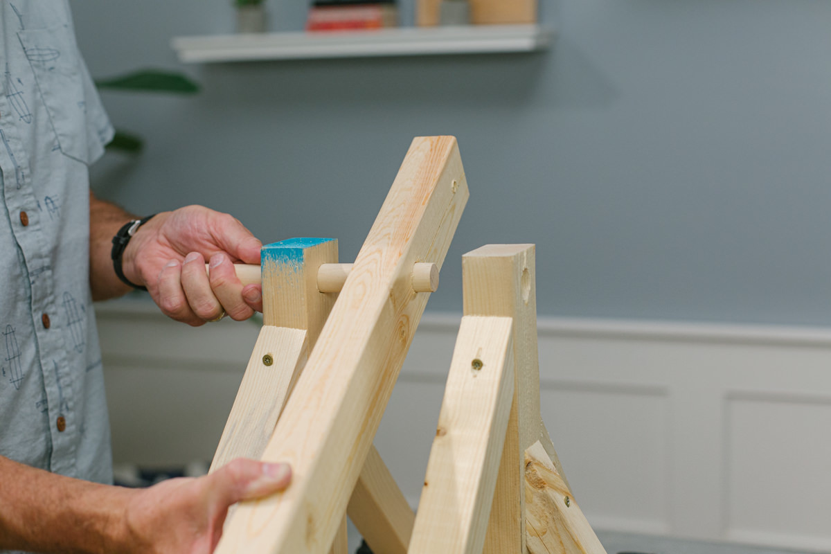 Pushing dowel rod through holes in sides and pivot arm of DIY wooden mini trebuchet assembly.