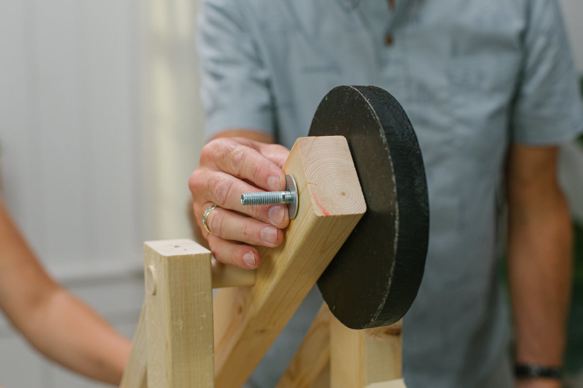 Disc weight attached to one side of DIY wooden mini trebuchet pivot arm, with end of hex bolt sticking out the other side and a washer attached.