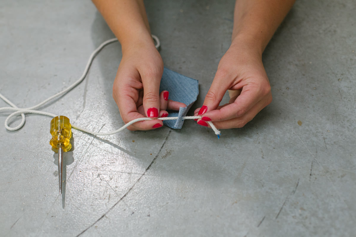 Threading cotton cord through folded end of DIY wooden mini trebuchet denim sling