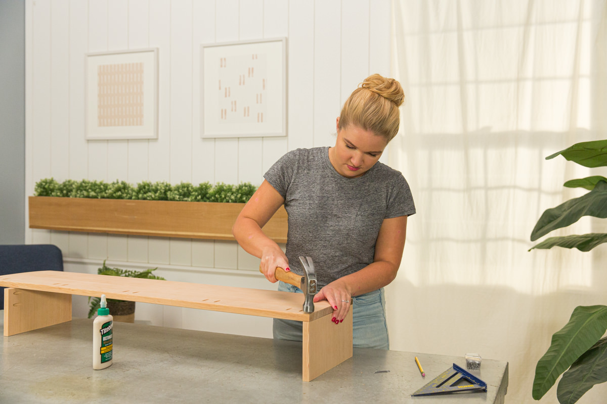 Connecting doug fir boards at right angle with hammer and nail to create corner of wood DIY coffee table assembly.