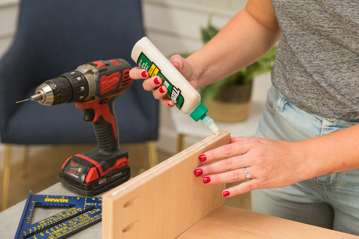 Applying wood glue to edge of short side of wood DIY coffee table box assembly.