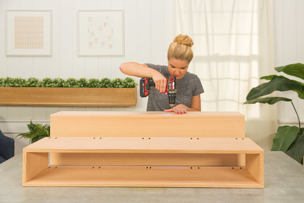 Pre-drilling back board of wood DIY coffee table assembly with power drill.