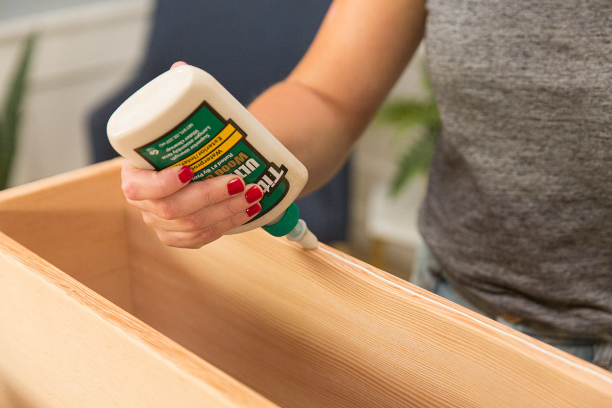 Applying wood glue to edge of open end of wood DIY coffee table assembly.