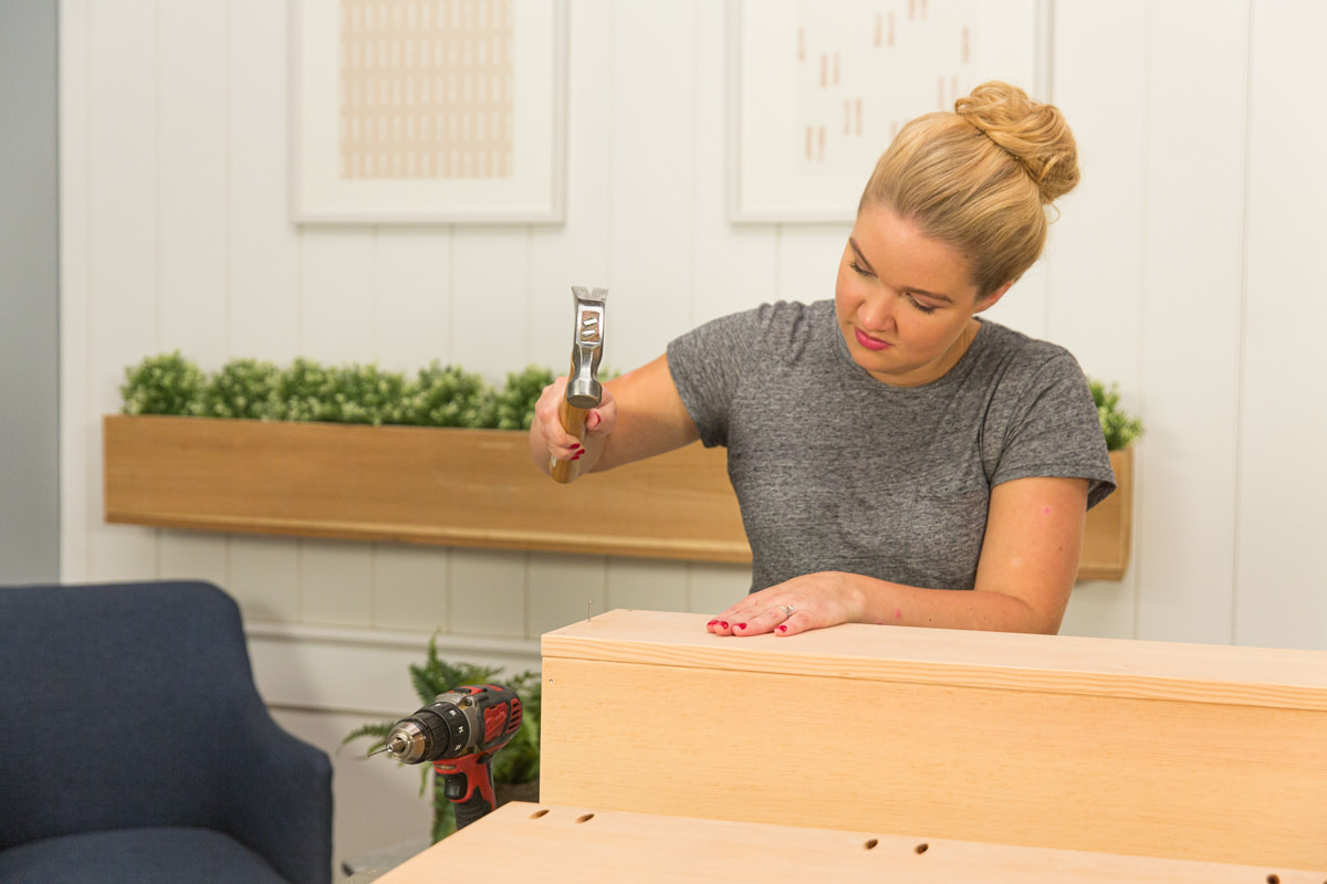 Hammering nails to attach back board to wood DIY coffee table assembly.