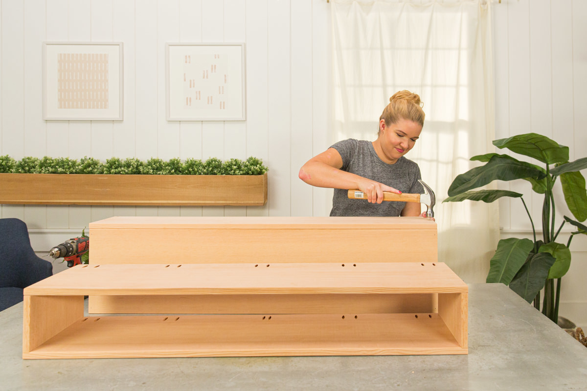 Hammering nails to attach back board to wood DIY coffee table assembly.