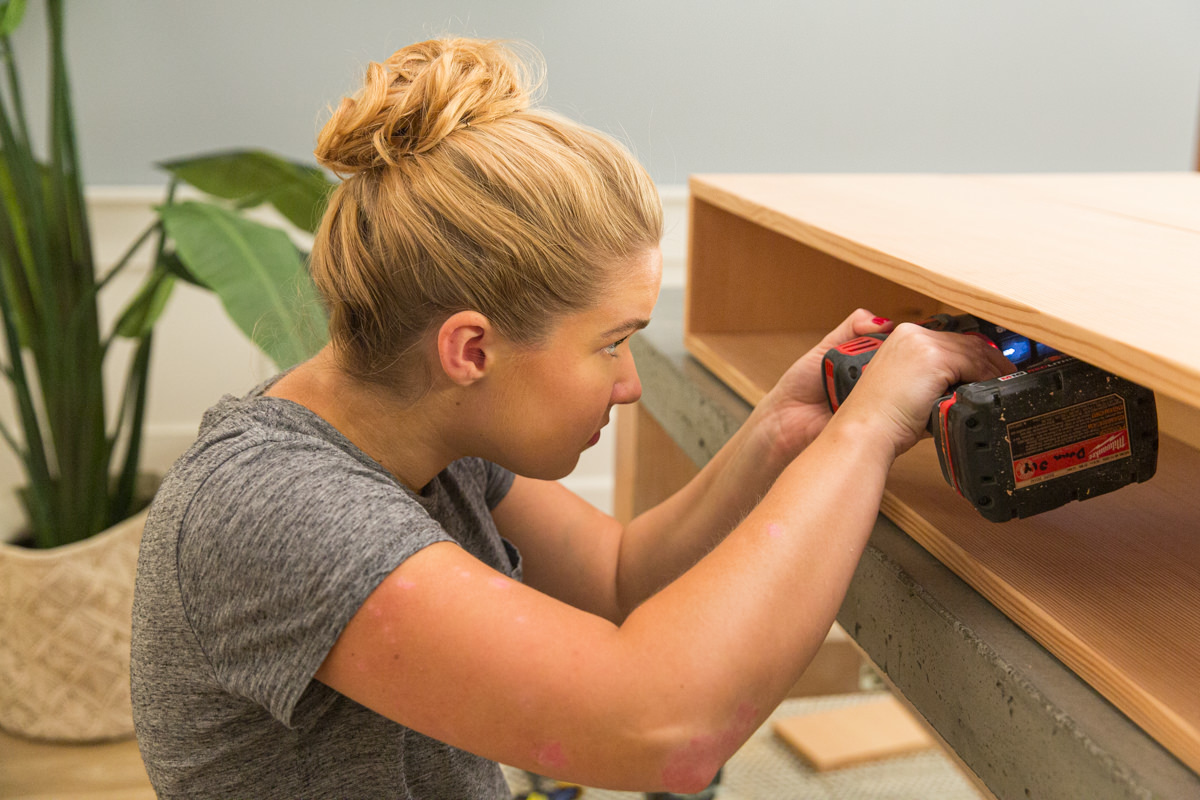 Driving screw with power drill to attach two halves of wood DIY coffee table assembly.