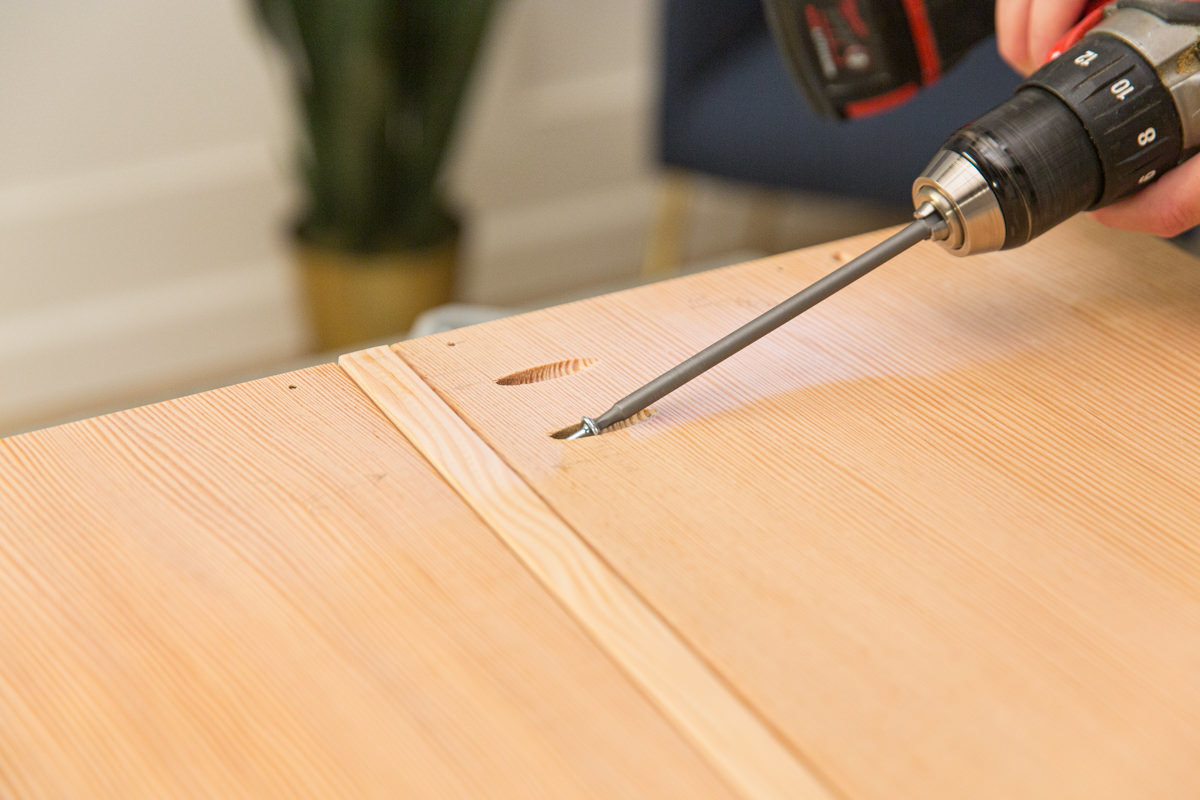 Driving screw with power drill to attach two halves of wood DIY coffee table assembly.