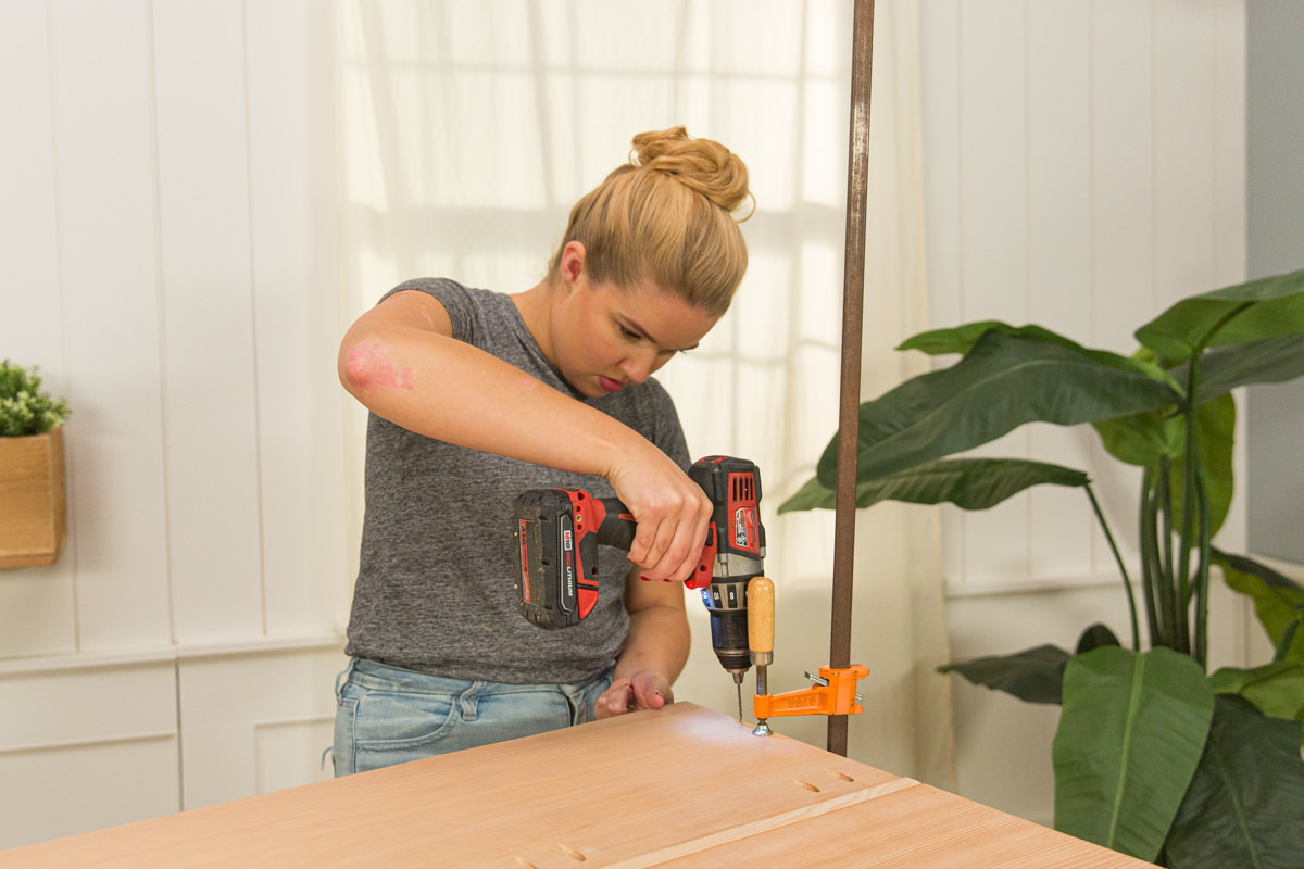 Driving screw with power drill to attach two halves of wood DIY coffee table assembly.