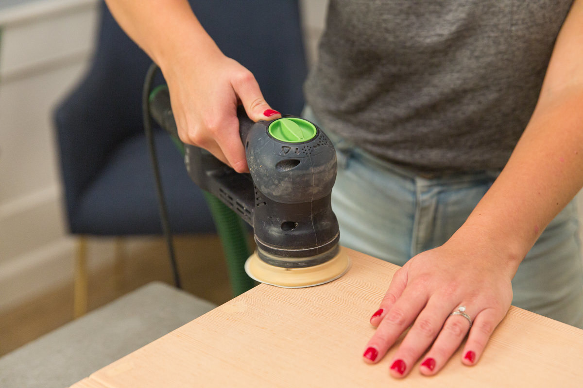 Sanding wood DIY coffee table assembly with power sander.