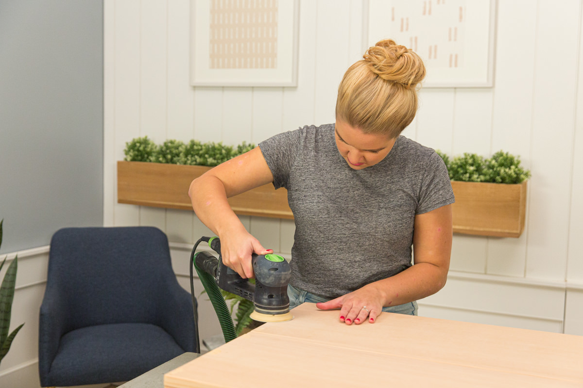 Sanding wood DIY coffee table assembly with power sander.