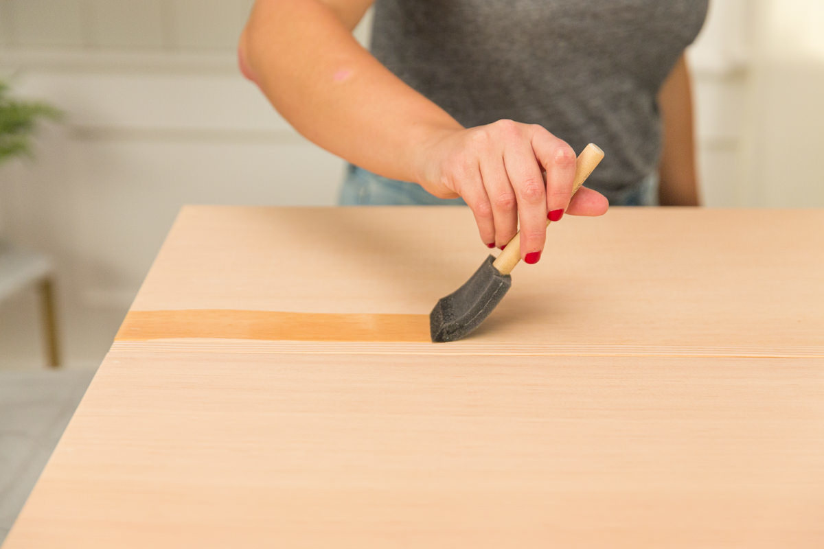 Applying wood conditioner to wood DIY coffee table assembly with foam brush.