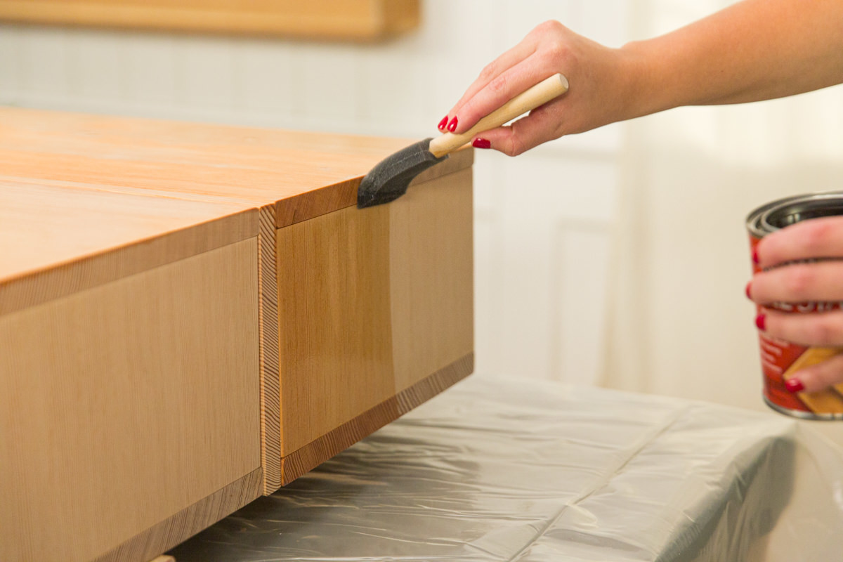 Applying wood conditioner to wood DIY coffee table assembly with foam brush.