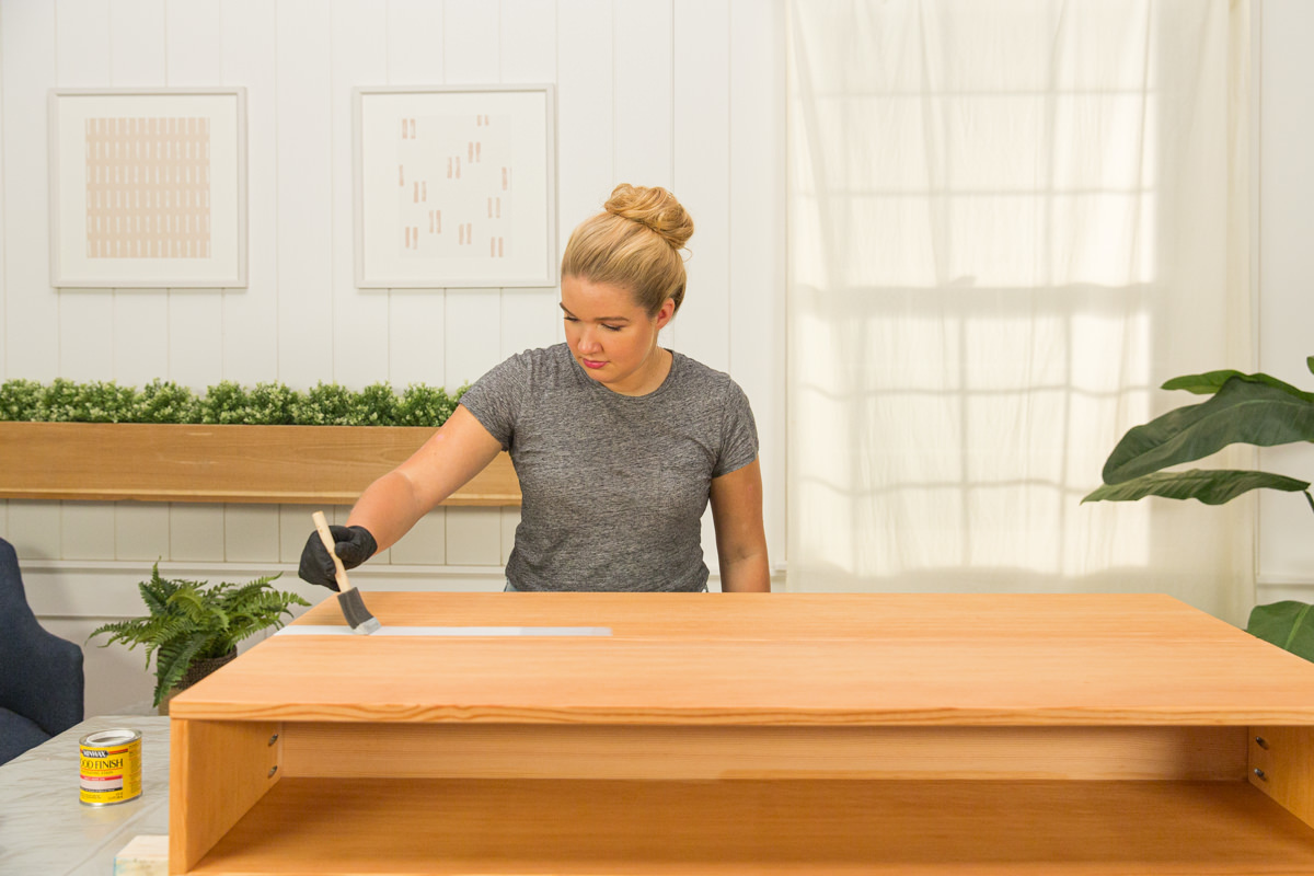 Applying wood stain to wood DIY coffee table assembly with foam brush.