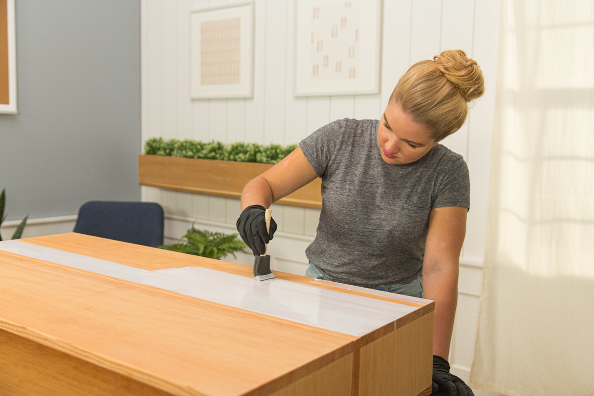 Applying wood stain to wood DIY coffee table assembly with foam brush.