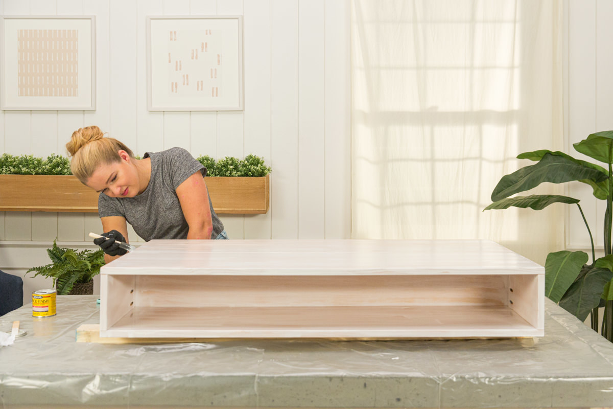 Applying wood stain to wood DIY coffee table assembly with foam brush.