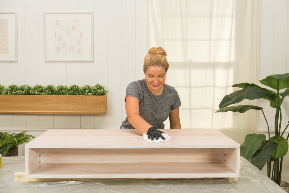 Wiping excess wood stain from wood DIY coffee table assembly with rag.