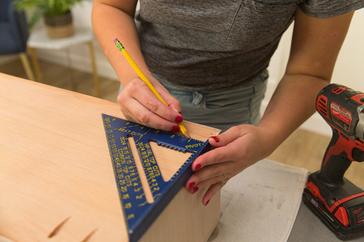 Measuring and marking wood DIY coffee table assembly with speed square and pencil.