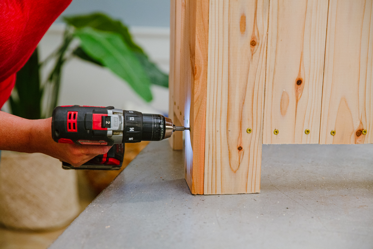 Driving screw with power drill to attach side panel to end of wood DIY elevated planter box assembly.