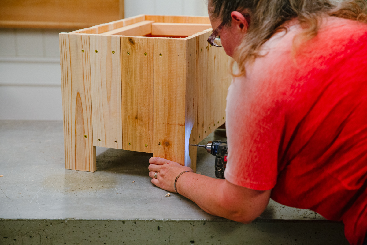 Driving screw with power drill to attach final end of wood DIY elevated planter box assembly.