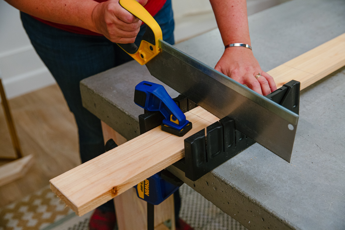 Cutting clamped and marked board with hand saw and miter box. 