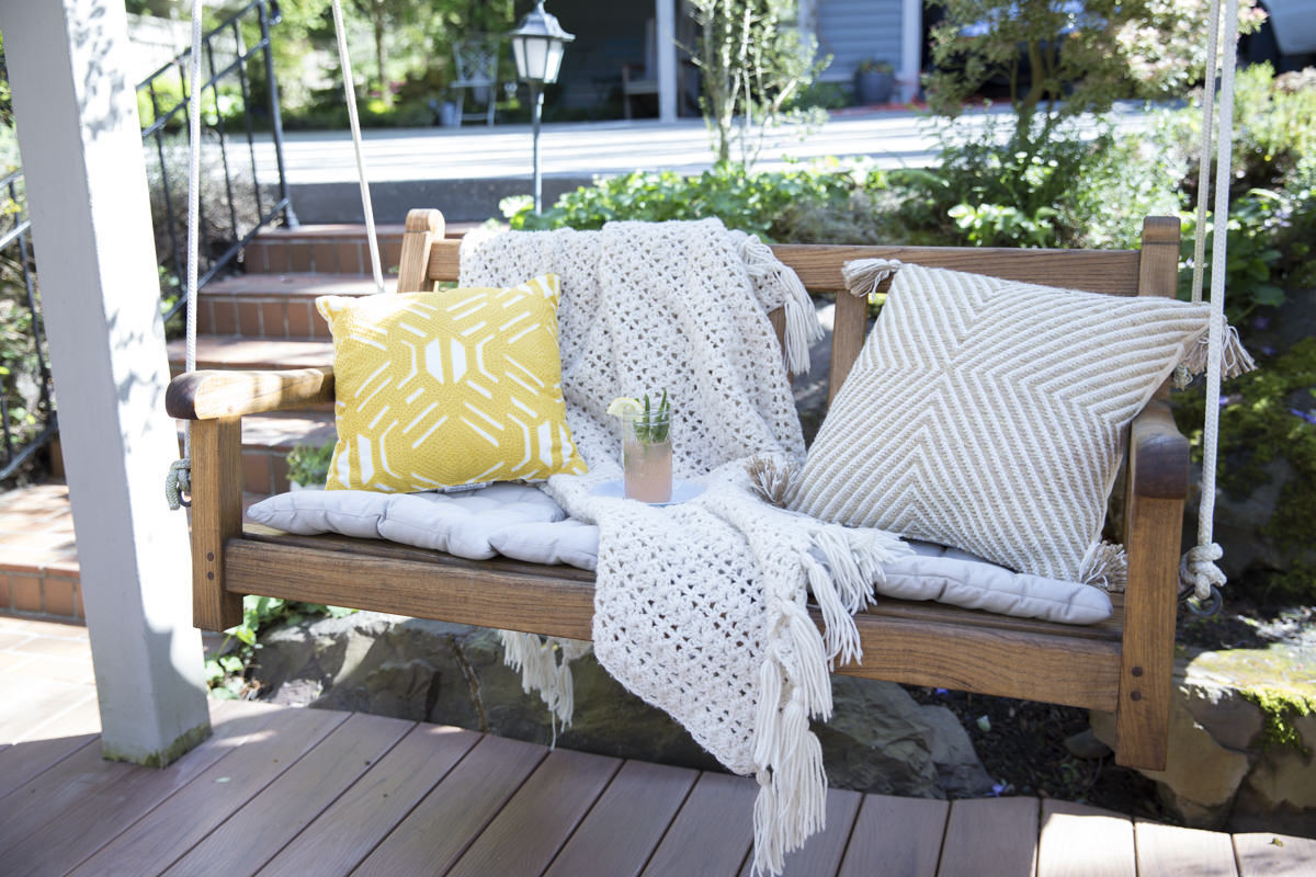 Wood DIY porch swing covered in blankets and pillows and stained with teak oil.