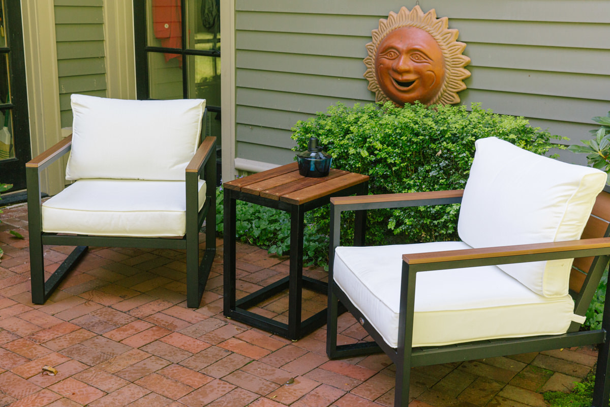 Cushioned outdoor chairs on either side of a wood DIY patio side table, which is stained with Penofin Hardwood Ipe.