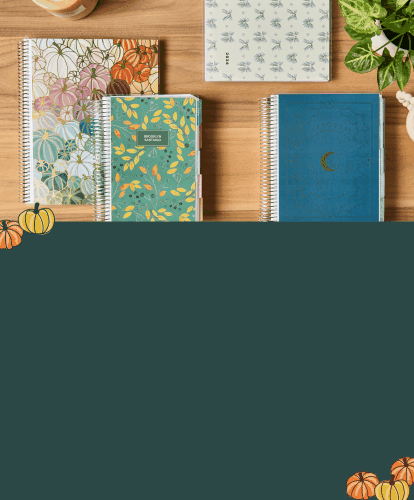 assorted coiled lifeplanners and notebooks featuring new holiday designs on a wooden desk with accessories.