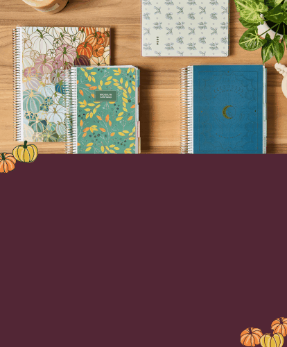 Assorted coiled planners featuring new fall holiday designs on a wooden desk with accessories. Click to shop Fall Flash Sale.