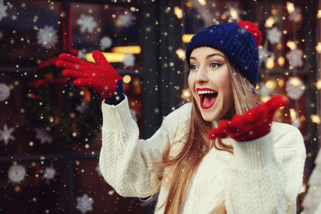 Street portrait of young beautiful woman acting thrilled, wearing stylish knitted clothes. Model expressing joy and excitement with hands and face. Festive garland lights. Snowfall effect. Close up. Street portrait of young beautiful woman acting thrilled, wearing stylish knitted clothes. Model expressing joy and excitement with hands and face. Festive garland lights. Snowfall effect. Close up.