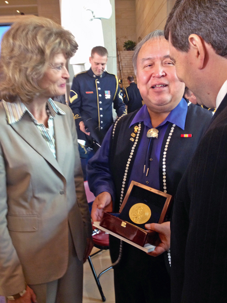 Ozzie-Sheakley Ozzie Sheakley hold the Congressional Gold Medal awarded to the Tlingit Tribe for code talking service during World War II. He speaks to Sens. Lisa Murkowski and Mark Begich after the ceremony. Photo by Liz Ruskin, APRN – Washington DC.