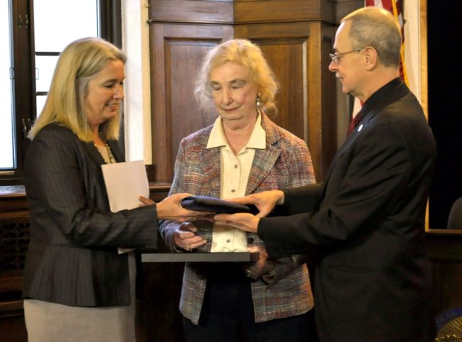 Rep. Cathy Munoz and her mother, Sally Engstrom, are given the flag that flew above the capitol in November when her father died. Rep. Mike Hawker organized the presentation. (Photo by Skip Gray / Gavel Alaska.)
