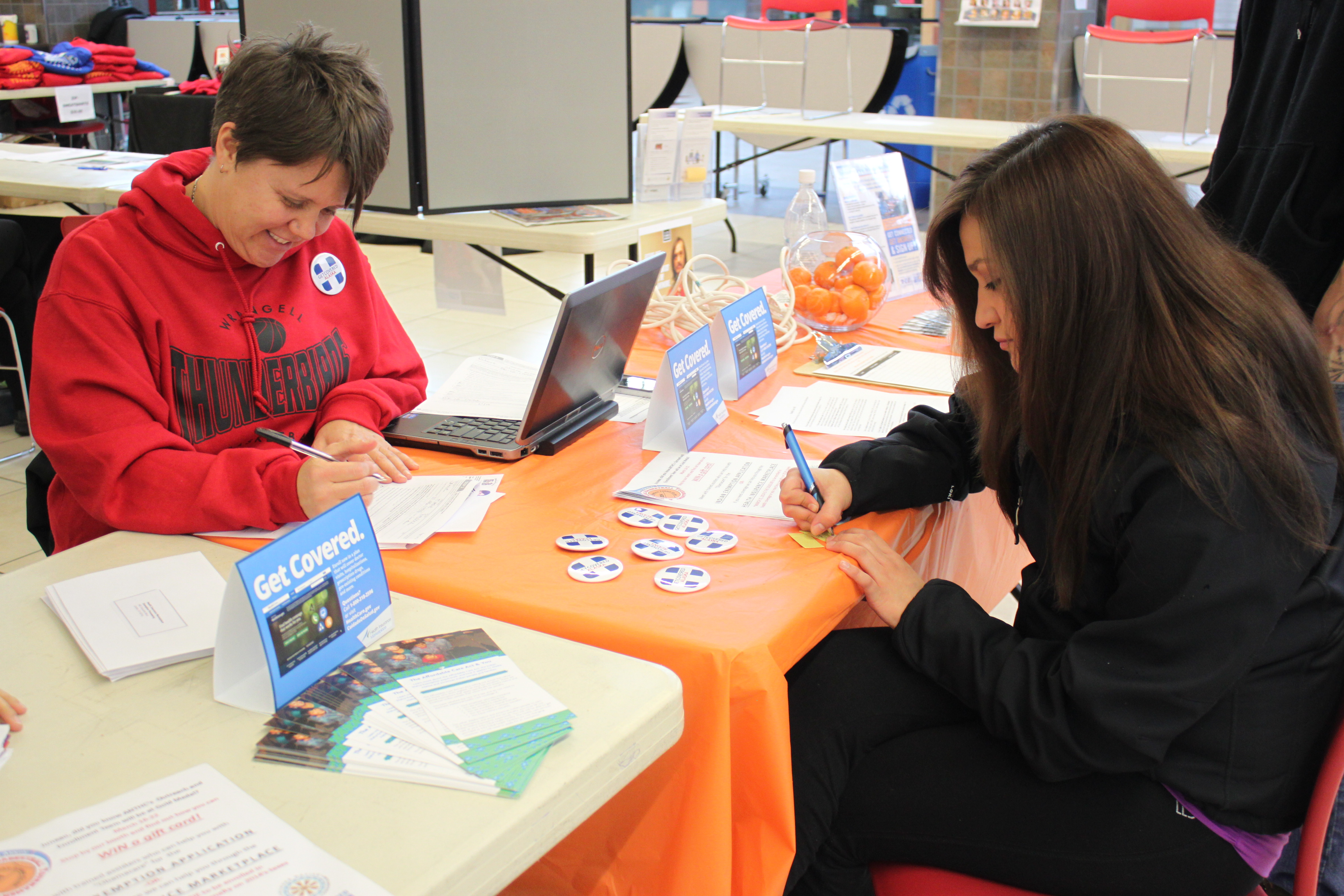 Alaska Native Tribal Health Consortium's Monique Martin helps Hoonah resident Jamie Paddock fill out an Indian Status Exemption form at the Gold Medal Basketball Tournament. (Photo by Lisa Phu/KTOO)