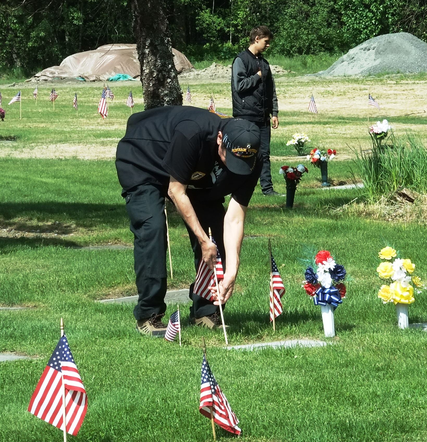 A veteran places a small flag near a grave stone on Memorial Day at Alaskan Memorial Park on Riverside Drive in Juneau. (Photo by Rosemarie Alexander/KTOO)