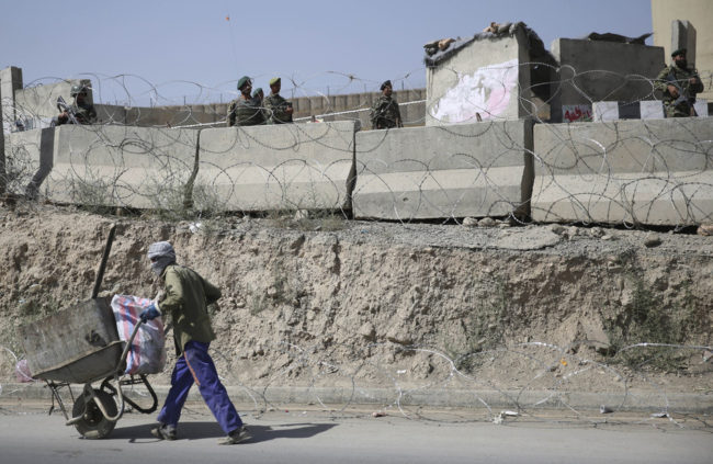 An Afghan laborer walks past a gate of Camp Qargha as Afghanistan National Army soldiers stand guard, west of Kabul, Afghanistan on Tuesday. Massoud Hossaini/AP