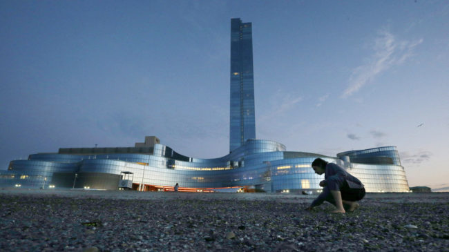 A woman gathers shells along the ocean near the Revel Hotel Casino in Atlantic City, N.J., early Tuesday. The casino resort has closed, a little over two years after opening with the promise of helping to renew Atlantic City. Mel Evans/AP