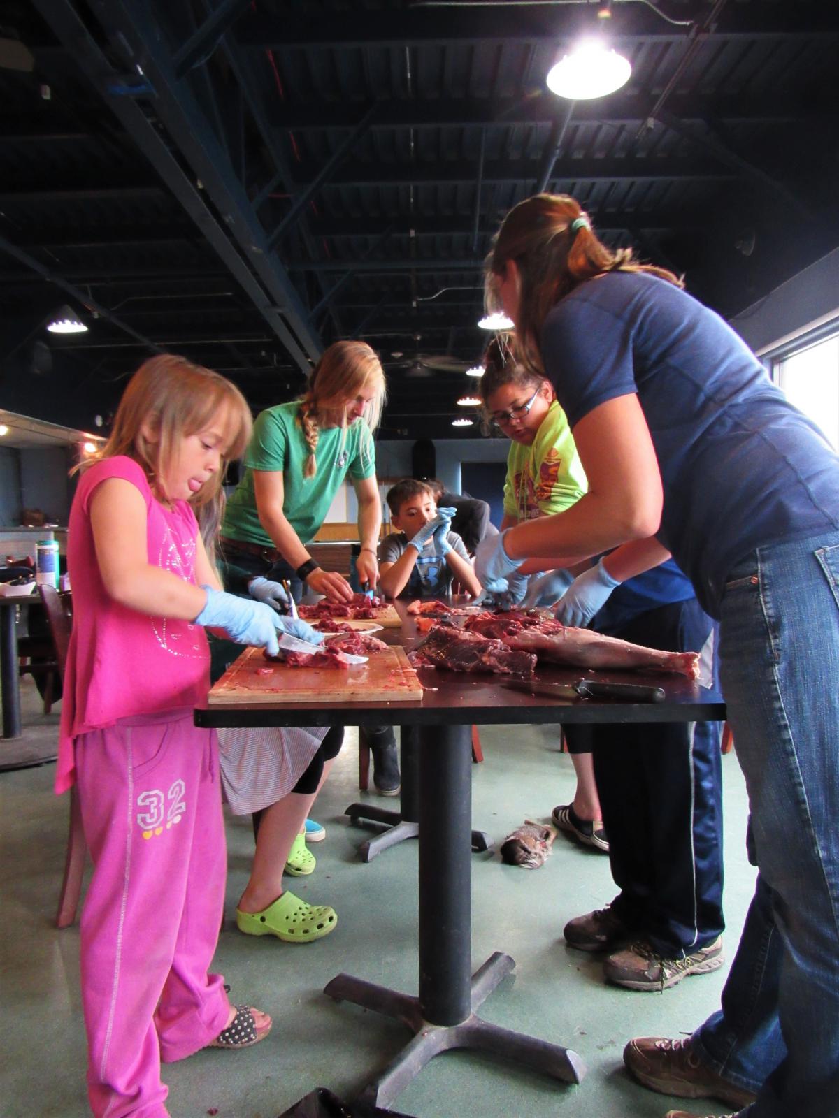 Instructors Lauren Divine and Erin Carr demonstrate how to process a hind shank at St. Paul’s reindeer camp. (Photo by Laura Kraegel/KUCB)