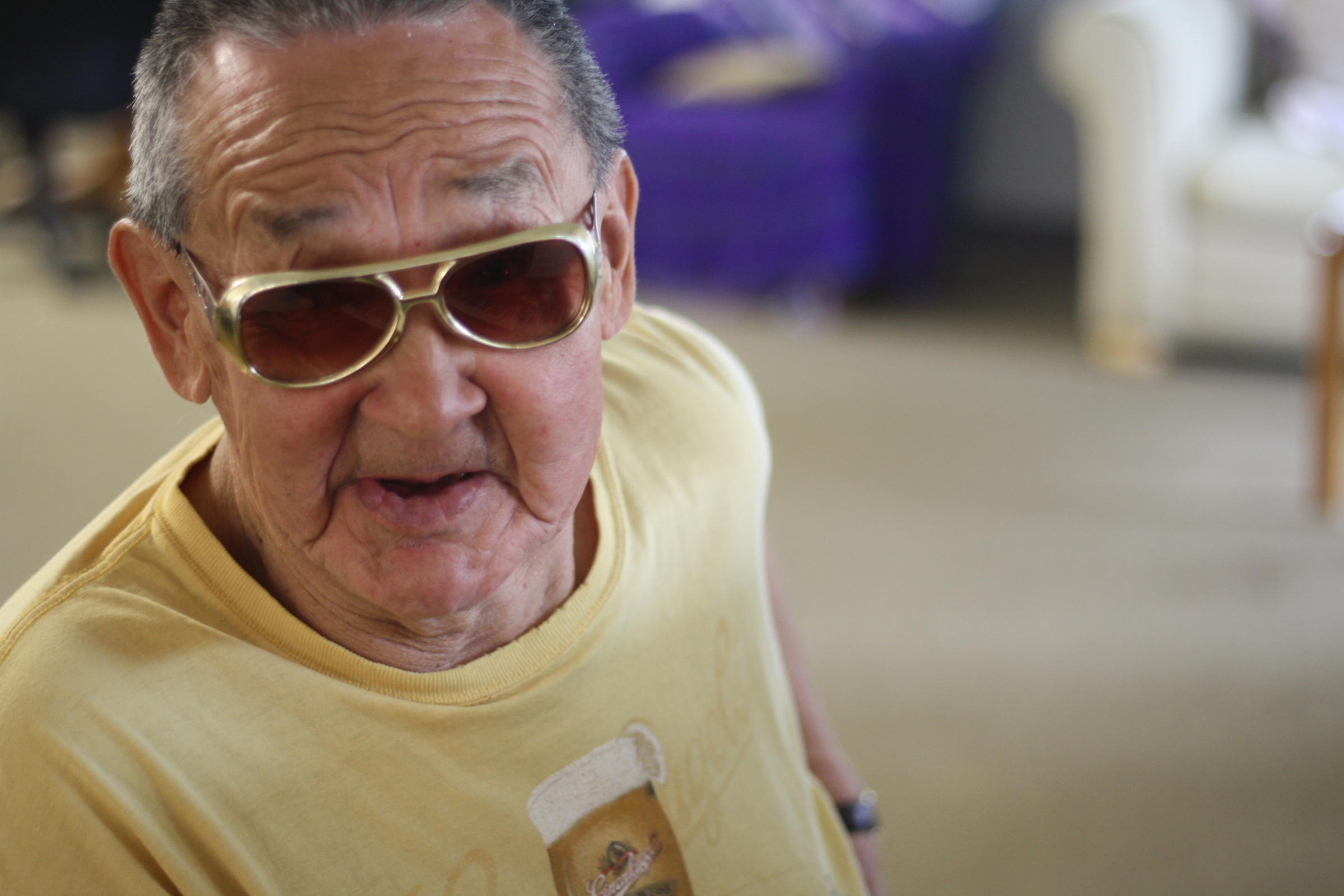 Paul “Elvis” Chythlook dons a pair of gold chrome shades at the piano bench. He plays for the community in the Dillingham Senior Center regularly, gospel and traditional tunes he knows by heart. (Photo by Zoey Laird/KDLG)