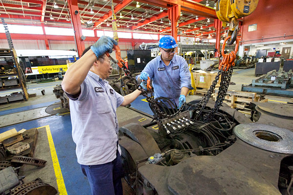 BL#5 Fuyuong Chung, a la derecha, y Josue Moir se preparan para levantar el carro que sostiene las llantas de los trenes para ser instaladas en un vagón del tren ligero.