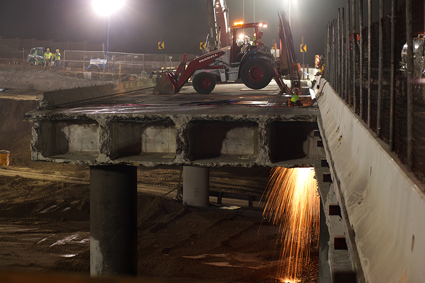 Looking east, sparks can be seen from the span over the I-405’s northbound lanes. Sparks result from a worker cutting steel reinforcements (rebar) under the bridge deck. Photo by Josh Southwick. Looking east, sparks can be seen from the span over the I-405’s northbound lanes. Sparks result from a worker cutting steel reinforcements (rebar) under the bridge deck. Photo by Josh Southwick.