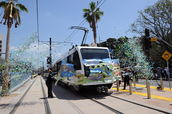Expo break-thru Operator Carolyn Kelly is at the controls of the inaugural train at the opening of the Expo Line. Operator Sheila Celestain, at left, is holding the banner. Barely visible, holding banner at right, is the third original Expo Line operator, Narvolean Jackson.