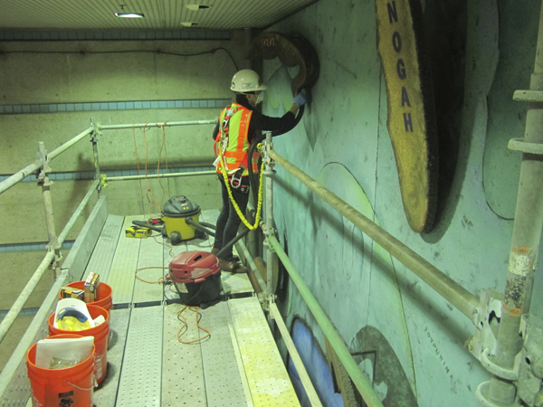 Specialized Metro Art staff work on the mural from a temporary scaffolding above escalators to contain dust particles, and not hinder the flow of transit patrons below.